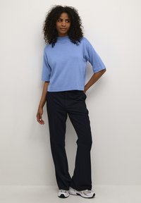 Top corto azzurro chiaro con un collo alto e maniche corte, abbinato a pantaloni a gamba larga blu navy e sneakers bianche.