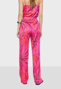 Roze satijnen jumpsuit met bloemenpatroon, dunne bandjes en een wijde pijpdesign. Opvallende oranje en blauwe accenten verbeteren het levendige bloemenmotief.