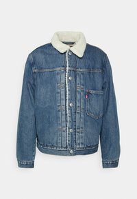 Jeansjacka med blå tvätt, med en vit sherpa-fodrad krage, knappstängning och ett bröstfack. Klassisk passform och sömnadsdetaljer.