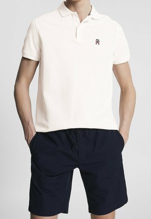 Polo beige clair à manches courtes, avec une texture subtile et un petit logo marine sur la poitrine ; assorti à un short marine.