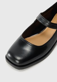 Black leather Mary Jane shoe with square toe, single strap across instep, and tan cushioned insole on a white background.