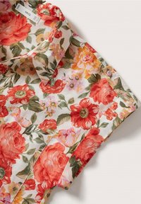 Chemise à manches courtes florale avec des fleurs rouges, orange et roses et des feuilles vertes sur fond blanc, avec col et bouton visibles.