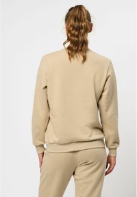 Beige sweatshirt med långa ärmar och ribbade muddar. Mjuk, slät textur. Rund hals och avslappnad passform, i kombination med matchande byxor.