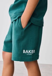 Zelené bavlnené šortky so bočnými vreckami, s bielym logom "BAKER". Materiál je hladký a má voľný strih.