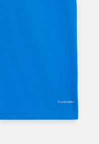 Camisa desportiva azul feita de um tecido liso e que afasta a humidade. Apresenta um logótipo na barra inferior. A barra está costurada de forma limpa.