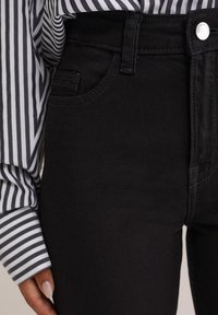 Čierne nohavice s vysokým pásom, s piatimi vreckami, s hladkou textúrou a jemným prešívaním, v kombinácii s pruhovanou blúzkou s dlhým rukávom.