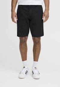 Shorts noirs en matériau léger, avec une coupe droite, des coutures discrètes et deux poches latérales. Associés à des baskets blanches.