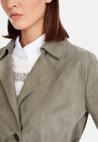 Gray suede jacket with a notched collar and visible stitching details, paired with a white sweater visible beneath the collar.