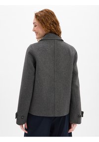 Grijs wollen jasje met een opstaande kraag, lange mouwen en knoopmanchetten. Heeft een getailleerde pasvorm en een gestructureerde stof.