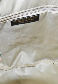 Echte leren binnenkant van een tas, met een gladde, lichtgekleurde stof met een ritssluiting en een label waarop staat "Echt leer, gemaakt in Italië."