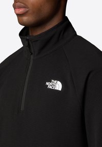 Pullover in pile nero con zip, in tessuto testurizzato, colletto alto e logo bianco sul petto sinistro. Presenta una chiusura frontale a mezza zip.