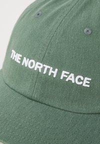 Zeleni platneni šešir s bijelim vezom logotipa "THE NORTH FACE" na prednjem panelu i šivenim ventilacijskim rupama.