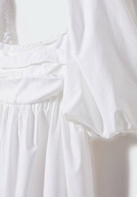 Weißes Kleid mit kurzen Puffärmeln, einer gerafften Taille und geschichteten Stoffdetails. Hergestellt aus leichtem Baumwollstoff mit glatter Textur.