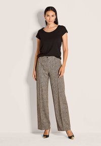 Zwarte korte mouwen top gecombineerd met bruine houndstooth wijde broek. Schoeisel is gemaakt van zwarte stof met gouden accenten.