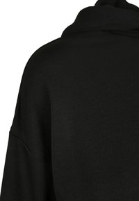 Suéter de punto negro con una textura suave, que presenta un corte relajado y un cuello alto. El diseño incluye un ligero brillo y detalles de costura mínimos.