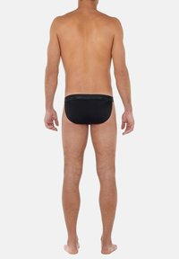 Slip da bagno neri con design uniforme e una cintura texturizzata a contrasto, taglio aderente e copertura minima, mostrato da dietro.