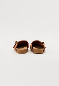 Brown suede backless sandals with a cork insole, low wooden heel, and adjustable strap decorated with a double metal buckle.