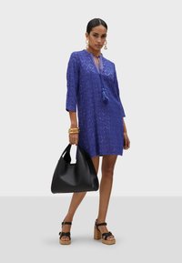 Blå tunika klänning med diamantmönster, trekvartsärmar och fransdetalj. Svart hobo-väska och sandaler med plattform och remmar fulländar looken.