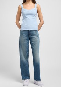 Light blue ribbed tank top with wide straps and a frilled neckline, paired with medium-wash, loose-fit denim jeans and white sneakers.