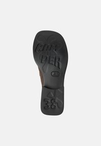Black rubber shoe sole with embossed "CAMPER" and size "38", featuring a textured surface and distinct tread pattern.
