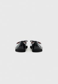 Chaussures en cuir verni noir avec une finition lisse, bout rond, lacets, et doublure intérieure rouge contrastante. Semelles plates.