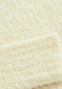 Texturiertes Creme-Gewebe mit einer weichen, flauschigen Oberfläche, das ein dezentes, gewebtes Muster in variierenden Farbtönen von hellem Beige aufweist.