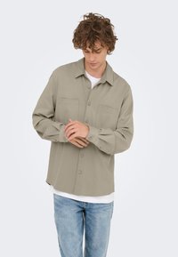 Overhemd met kraag en knopen in licht beige, gemaakt van zachte stof. Voorzien van twee borstzakken en lange mouwen, gedragen over een wit T-shirt.