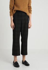 Černé kalhoty s širokými nohavicemi a károvaným vzorem zvýrazněným červenými akcenty, nošené s černými mokasíny.