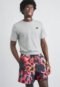 Γκρι μπλουζάκι Nike σε συνδυασμό με πολύχρωμο σορτς με αφηρημένο μοτίβο σε αποχρώσεις μαύρου, ροζ και πορτοκαλί. Διαθέτει ελαστική μέση.