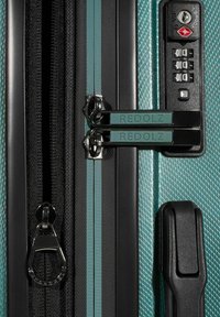 Hard-shell turquoise koffer met diagonaal textuurpatroon, zwarte rits en slot, dubbele rood-zwarte ritstrekkers met het label "REDOLZ".