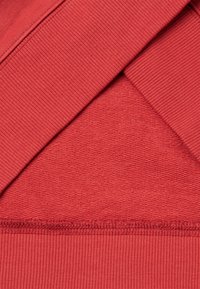 Gros plan sur un tissu rouge côtelé plié montrant la texture tricotée et les détails de l'ourlet cousu.