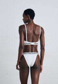 Wit lingerie set met een beha met dunne bandjes en een merkband, gecombineerd met bijpassende stringonderbroek, beide gemaakt van zachte stof.