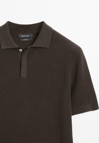 Polo marrone scuro in cotone strutturato, con colletto e un solo bottone al collo. Etichetta del marchio visibile all'interno del colletto.