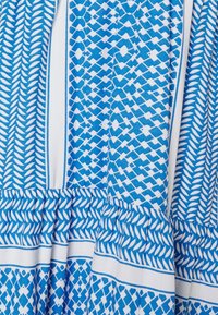 Tela de patrón azul y blanco con diseños geométricos, con un fondo fruncido y rayas en contraste a lo largo de los bordes.