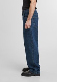 Blauwe denim straight-leg jeans met een hoge taille, vijf-pocket ontwerp en subtiele vervaging. Draag ze met zwarte schoenen. Zijaanzicht.