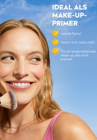 Makeup-Primer mit leichter Textur, nicht fettende Formel. Nahaufnahme eines Modells, das einen Pinsel gegen einen klaren blauen Himmel hält.