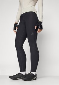 Zwarte sportleggings met een strakke pasvorm en zichtbare stiksels. Gepaard met zwarte fietsschoenen en vingerloze handschoenen, gedragen met een licht top.