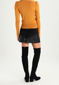 Senapsgul långärmad topp med puffiga axlar, i kombination med en svart minikjol i imitationsläder med ett diagonalt mönster. Svarta knähöga stövlar.