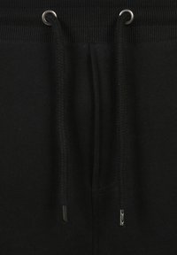 Zwarte sweatpants hebben een gestructureerde tailleband met metalen oogjes en gevlochten trekkoorden. De stof lijkt zacht en glad te zijn.