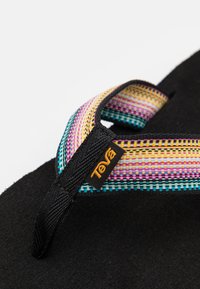 Teva-sandal med en bred, flerfarget stripet rem, svart teksturert såle og logopreget på remmen. Fokuserer på uformell utebekledning.