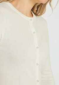 Ljuscremefärgad cardigan i mjukt stickat material. Har rund halsringning och pärlknappar längs med framsidan. Slen textur.