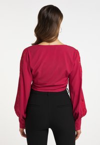 Rød bluse med lange, puffede ærmer med blonderdetaljer. Glat stof med rund halsudskæring og snøring på ryggen. Sammen med tætsiddende sorte bukser.