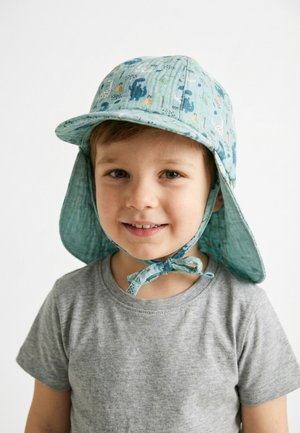 Lächelnder Junge, der einen blauen Sonnenhut mit Nackenschutz und Bindeband sowie ein graues T-Shirt trägt, vor einem schlichten weißen Hintergrund.