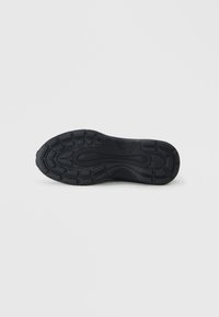 Black sneaker sole featuring textured rubber with a traction pattern. Rounded shape with raised accents for grip and stability.