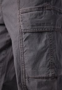Szare szorty cargo z teksturowanej tkaniny, wieloma kieszeniami i nadrukowaną etykietą "WEAR THE CODE" z boku. Prosty design i prosty krój.