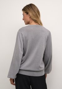 Grå tröja i pulloverstil med strukturerad yta, långa puffärmar och rundad halsringning. Nertill har den en lätt elastisk kant för en figurnära passform.