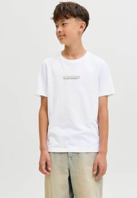 Witte katoenen t-shirt met korte mouwen, voorzien van een klein grijs logo-tekst "JACK & JONES" op de borst. Gekozen in combinatie met beige broeken.