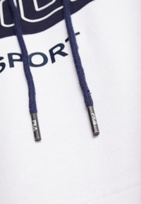 Sudadera blanca con estampado gráfico en marino, que presenta dos cordones en marino con puntas metálicas grabadas con "FILA". Textura de tela suave.