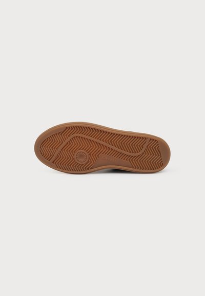 Semelle de chaussure marron avec motif de grip à chevrons texturé, empreinte circulaire du logo et le mot "VERSACE" visible au centre.