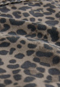 Tkanina s leopardím vzorom v odtieňoch béžovej a čiernej, s textúrovanou väzbou a nepravidelne tvarovanými škvrnami a jemným finišom.